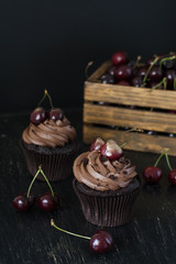Tasty chocolate cupcakes with cherries and a wooden box of cherries on a black background