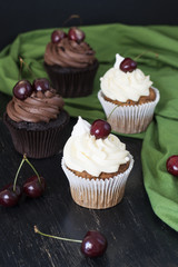 Delicious chocolate and vanilla cupcakes with cherries on a black background
