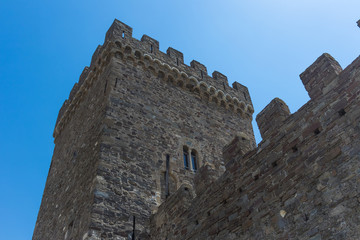 battlements, a window and walls of a tower of an ancient castle against a blue sky