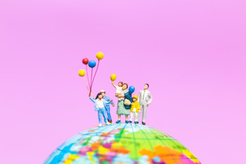 Miniature people : Happy family holding balloon on The globe with pink background