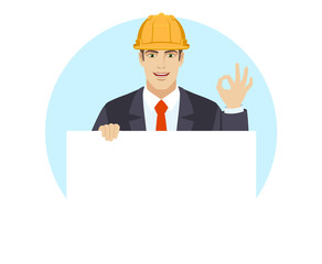 OK! Businessman in construction helmet holding white blank poster and showing a okay hand sign