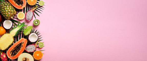 Exotic fruits and tropical palm leaves on pastel pink background - papaya, mango, pineapple,...