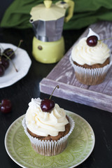 Vanilla cupcakes with cherries, a plate of berries and a coffee pot on a dark background