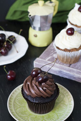 Vanilla cupcakes and chocolate cupcakes with cherries, a plate of berries and a coffee pot on a dark background