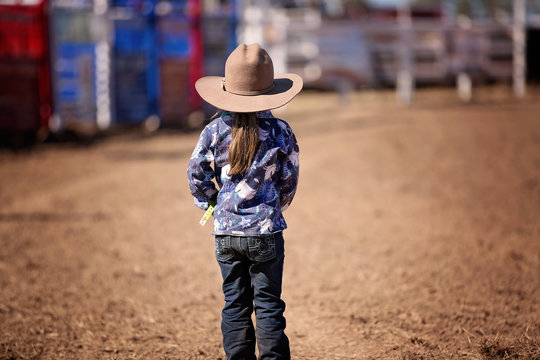 Little Cowgirl Stands In The Dust Watching A Country Rodeo