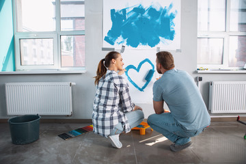 My darling. Alert caring woman smiling at her man and they painting a heart with her man