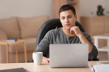 Young man working with laptop at table in home office