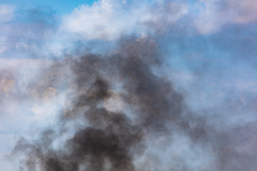 Black smoke against a blue sky with clouds