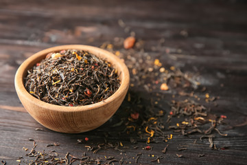 Bowl with dry tea on wooden background