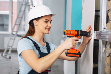 Feeling joyful. Content skilled builder wearing a uniform and working with a drill