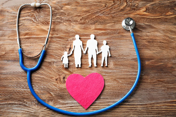 Family figure, heart and stethoscope on wooden background. Health care concept