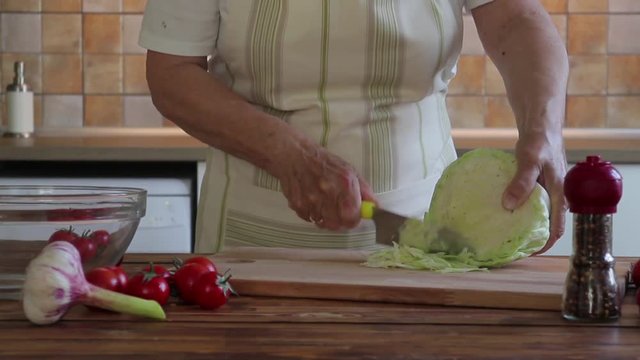 Hands of an elderly woman cutting the cabbage with a knife on a chopping board