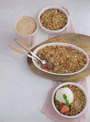 Strawberry and rhubarb homemade granola crumble with ice-cream and cup of cappuccino top view on white concrete background, copy space