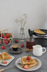 Breakfast table with fresh homemade waffles, honey, coffee and fresh strawberries