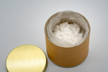 Sea salt in plastic bag kept in open recycled cylinder container by its golden lid isolated on white background.