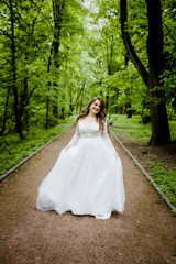 An magnificent bride in a white dress walks along the path in the park