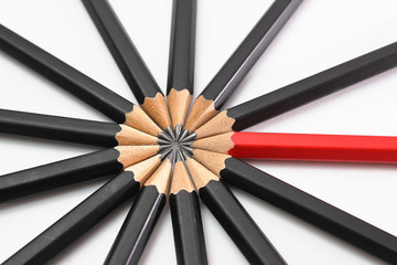 Red pencil standing out from crowd of plenty identical black fellows on white table. Leadership,...