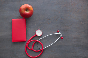Stethoscope with apple and notebook on grey background. Healthy food concept