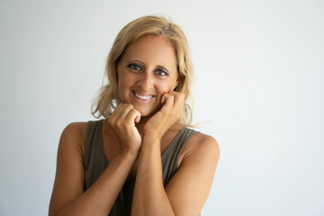 Fototapeta premium Cheerful blonde lady happy about new cosmetic product and smiling at camera. Closeup of attractive Caucasian woman keeping hands at face and posing. Positive emotions and skin care concept