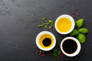 Obraz na płótnie Canvas Soy sauce, olive oil and balsamic sauce with herbs basil, parsley, pepper and thyme in white ceramic bowls on black stone or concrete background.