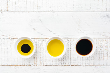 Soy sauce, olive oil and balsamic sauce in ceramic bowls on white wooden background. Top view.