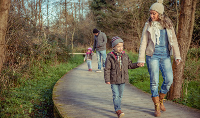 Fototapeta premium Happy family walking together holding hands over a wooden pathway into the forest