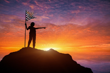 Silhouette of  woman holding a checkered flag on a mountain.