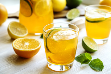 Iced lemonade pitcher & two glasses, wooden juicer, cold citrus infused water, lemon & lime, mint leaves, cutting board on white wooden windowsill. Apartment window background, close up, copy space.