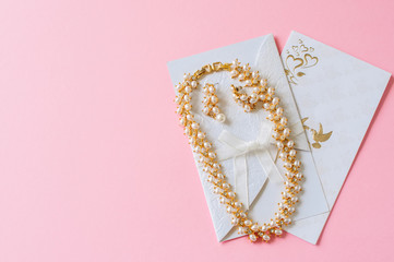 Wedding concept. Invitation cars and pearl necklace on a pink ba
