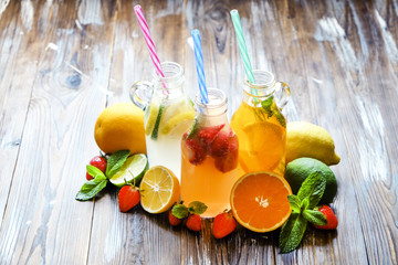 Three vintage bottles of fresh ice cold lemonade, different taste drinks w/ lemon, orange, grapefruit, lime, mint leaves & strawberry on grunged wooden table background. Top view, copy space, close up