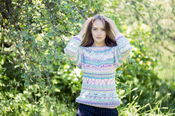 The blonde with blue eyes, in a knitted pullover, poses outdoors