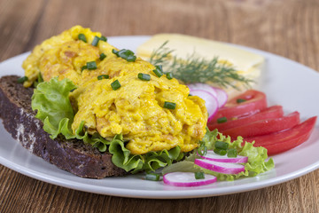 Egg omelette on a piece of black bread with red tomatoes, cheese and radish on a wooden table, close up