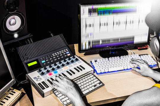 male producer hands composing music on midi keyboard, studio equipment and computer in studio