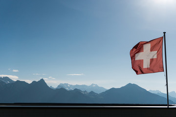 Swiss flag blowing in the wind with a gorgoues mountain landscape and blue sky behind
