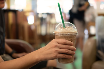 Woman holding plastic glass of iced coffee with milk