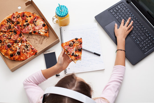 Young teenager girl working on a project while eating pizza - top view