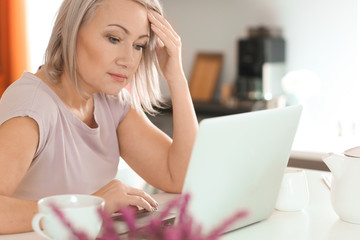 Mature woman reading news on laptop screen at home