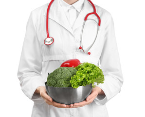 Female doctor holding bowl with healthy vegetables on white background