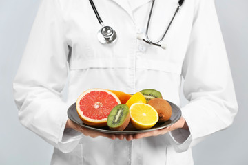 Female doctor holding plate with healthy fruits on white background