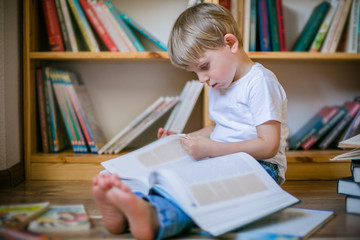 Boy reading a large book in front of book shelves