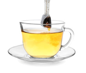 Brewing of hot beverage with tea bag in glass cup on white background