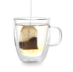 Brewing of hot beverage with tea bag in glass cup on white background
