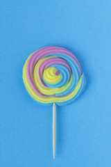 Creative view of colorful, handmade swirl lollipop in summer colors on blue paper background. Minimalism. Abstraction.