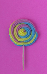 Creative view of colorful, handmade swirl lollipop in summer colors on pink paper background. Minimalism. Abstraction. Creativity.