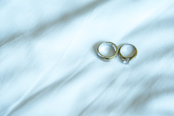 Wedding rings put on white bedspread with wrinkles.