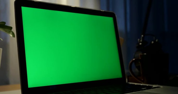 Laptop with green screen. Dark office. Dolly in . Perfect to put your own image or video.Green screen of technology being used. Chroma Key laptop