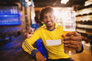 Cheerful football fan in jersey is saluting to the victory of his club with a pint of beer.