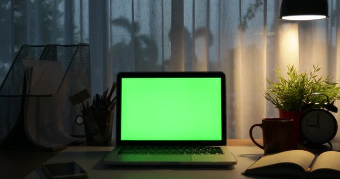 Laptop with green screen. Dark office. Dolly move left to right. Perfect to put your own image or video.Green screen of technology being used. Chroma Key laptop