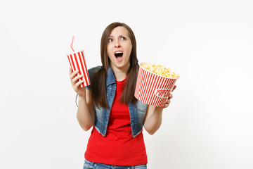 Obraz premium Portrait of young shocked irritated woman in casual clothes watching movie film, holding bucket of popcorn and plastic cup of soda or cola looking up isolated on white background. Emotions in cinema.