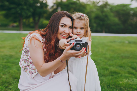Pretty woman in light dress and little cute child baby girl take picture on retro vintage photo camera in park. Mother, little kid daughter. Mother's Day, love family, parenthood, childhood concept.